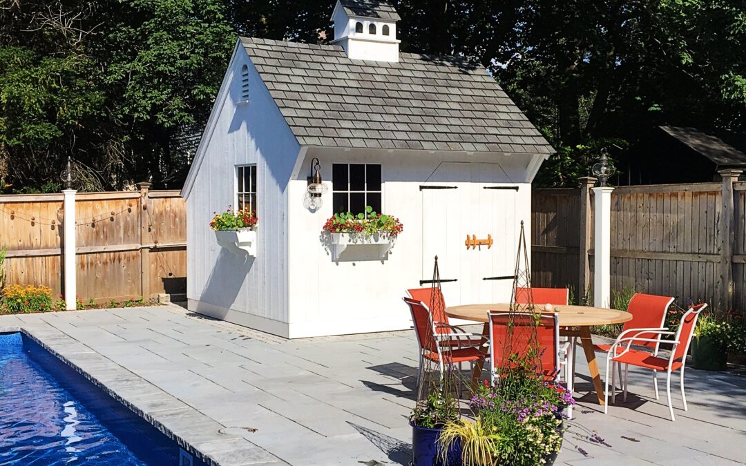 Beautiful, white Saltbox Pool shed with flower boxes and cupola sitting on concrete deck next to pool