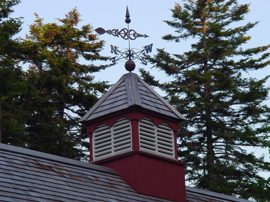 Red Cupola with weathervane and pine trees in background