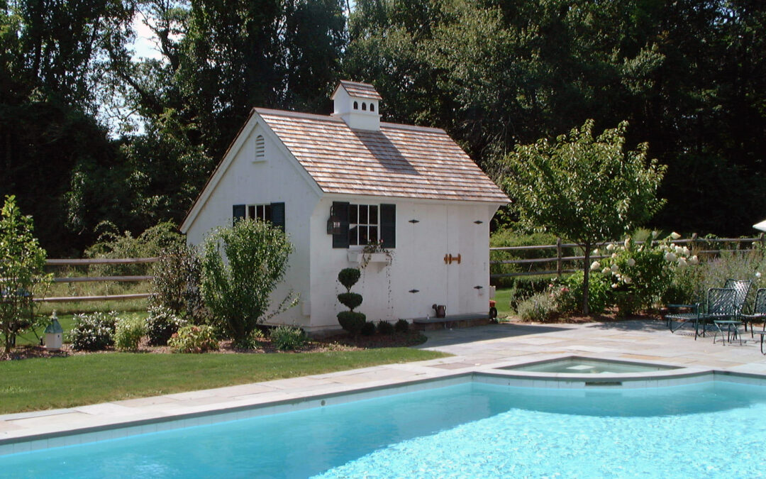 White Saltbox Pool House next to pool with plants and bushes all around
